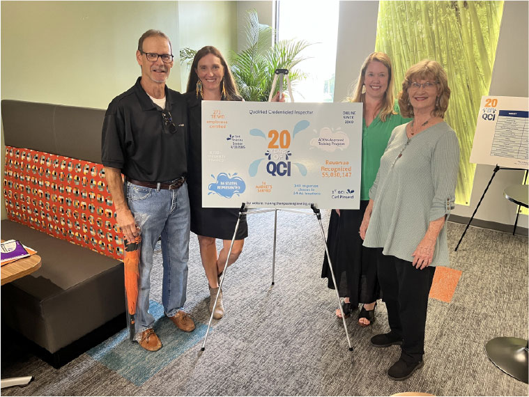 Four people stand by a 20 Years of QCI sign celebrating achievements in safety and certifications.