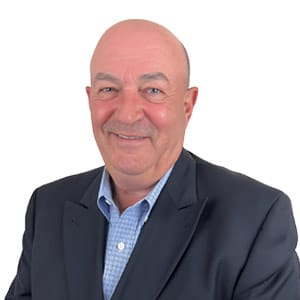 I'm unable to identify the individual, but here's a suitable alt text: Smiling man in a suit and blue shirt on a white background.