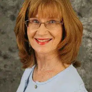 Smiling woman with glasses against a gray background.