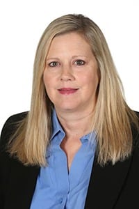 Portrait of a woman with long blonde hair wearing a blue shirt and black blazer, neutral background.