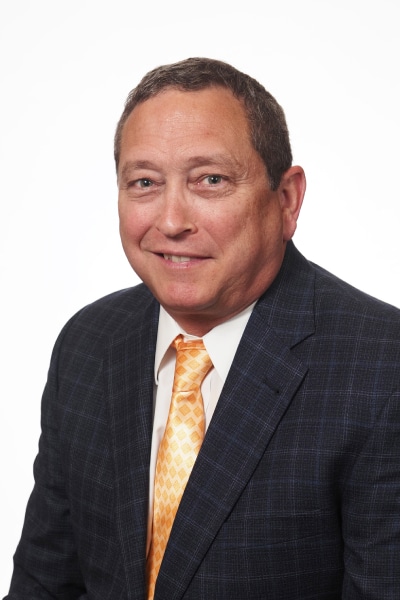 Man in a suit with a yellow tie, smiling, against a white background.
