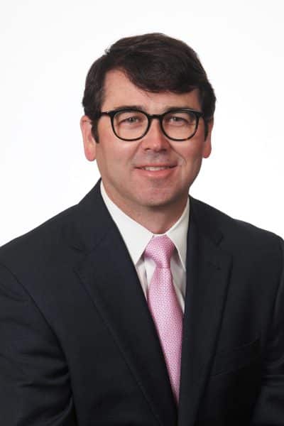 Man in suit and pink tie with glasses, professional portrait.